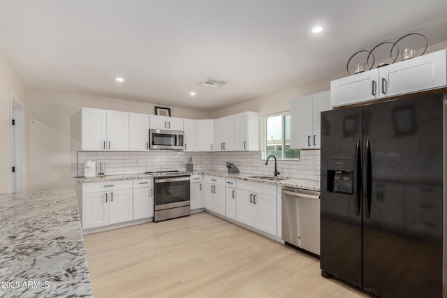 kitchen featuring decorative backsplash, visible vents, stainless steel appliances, a sink, and light wood-type flooring