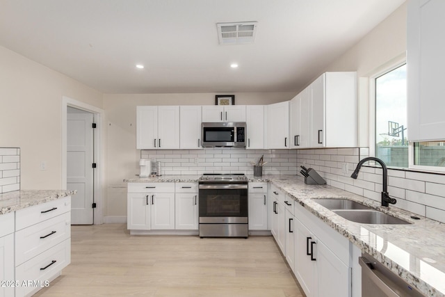 kitchen with a sink, light wood finished floors, white cabinetry, stainless steel appliances, and visible vents