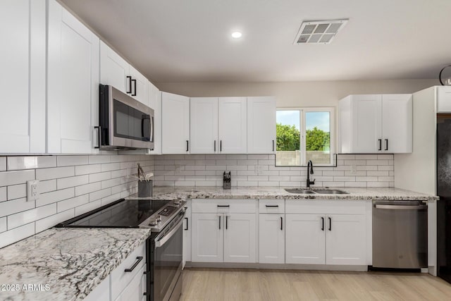 kitchen featuring visible vents, light wood finished floors, stainless steel appliances, white cabinetry, and a sink