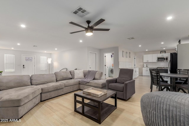 living area featuring light wood finished floors, visible vents, ceiling fan, and washer / dryer
