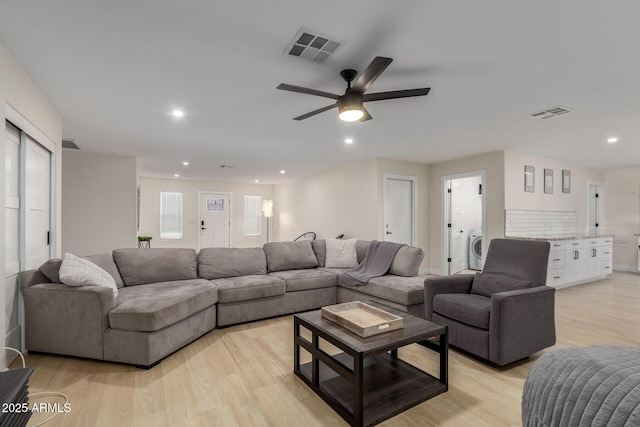 living room featuring a ceiling fan, washer / dryer, light wood finished floors, and visible vents