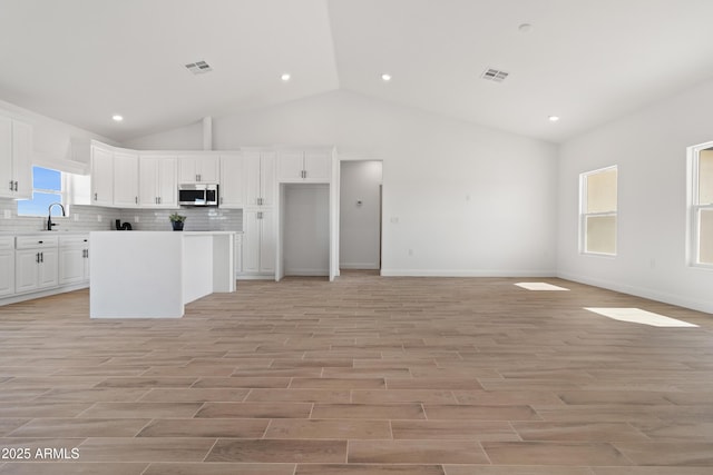 1222 S 365th Ave, Tonopah, AZ 85354 - kitchen featuring stainless steel microwave, lofted ceiling, white cabinetry, decorative backsplash, and light countertops
