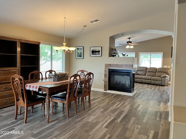 dining area with a tiled fireplace, wood-type flooring, lofted ceiling, and a healthy amount of sunlight