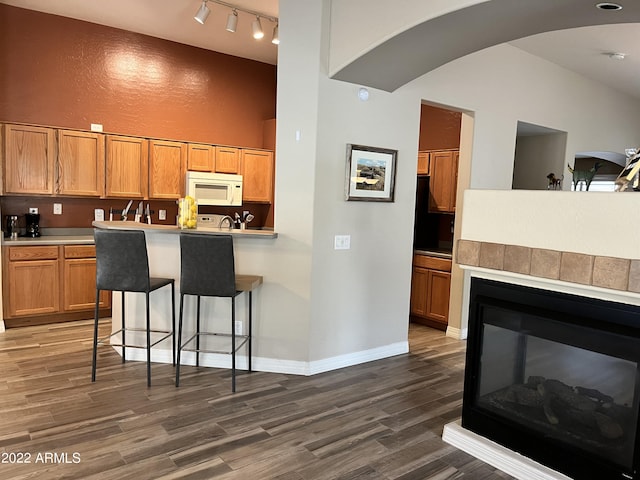 kitchen with a kitchen bar, rail lighting, high vaulted ceiling, a multi sided fireplace, and dark hardwood / wood-style flooring