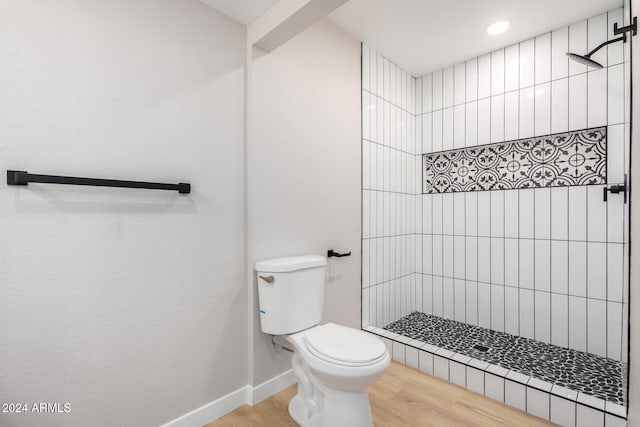 bathroom featuring wood-type flooring, tiled shower, and toilet