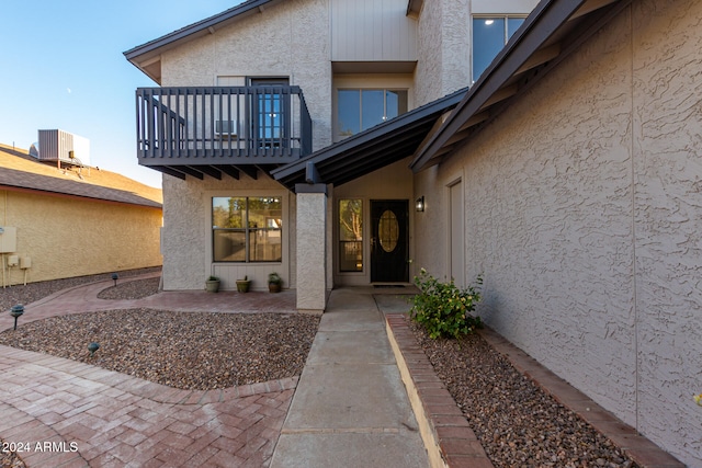 view of exterior entry with cooling unit, a balcony, and a patio area