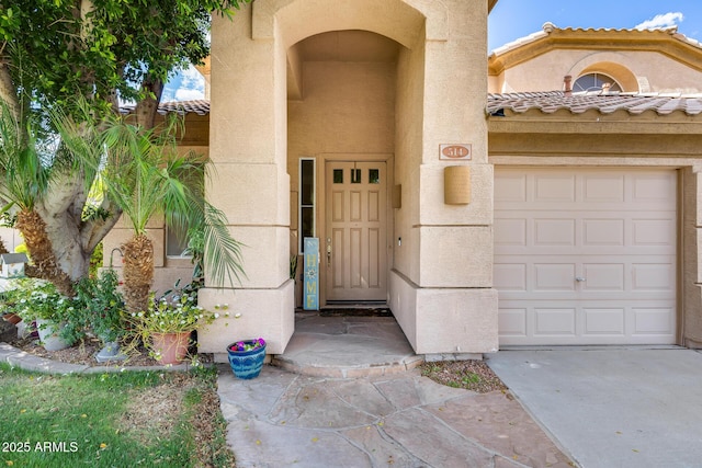 property entrance featuring stucco siding, concrete driveway, a garage, and a tiled roof