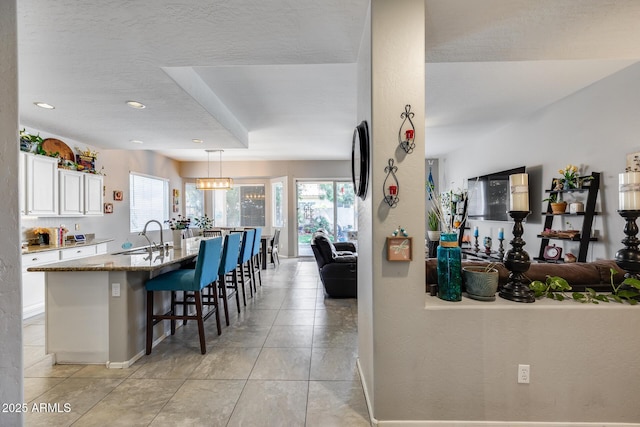 kitchen featuring a sink, open floor plan, a kitchen bar, white cabinetry, and baseboards