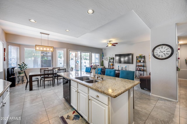kitchen with a sink, a textured ceiling, open floor plan, black dishwasher, and an island with sink