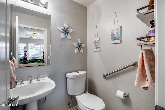 half bath with a sink, toilet, and a textured wall