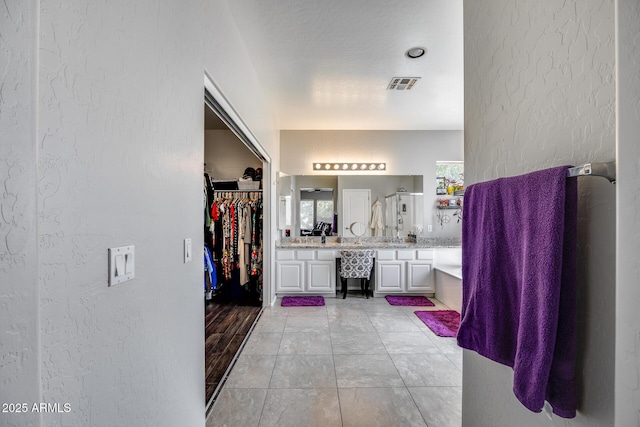 full bathroom with a textured wall, vanity, a walk in closet, and a shower