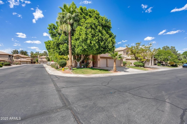 view of property hidden behind natural elements featuring a residential view, stucco siding, a tile roof, concrete driveway, and a garage