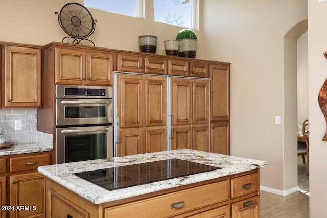 3507 N Snead Dr, Goodyear, AZ 85395 - kitchen with stainless steel double oven, black electric cooktop, brown cabinetry, arched walkways, and decorative backsplash
