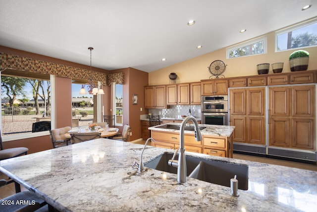 3507 N Snead Dr, Goodyear, AZ 85395 - kitchen featuring a sink, double oven, light stone counters, brown cabinetry, and hanging light fixtures