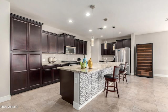 kitchen with appliances with stainless steel finishes, a kitchen bar, sink, hanging light fixtures, and a kitchen island with sink