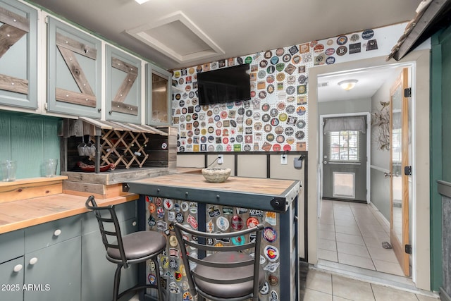 kitchen featuring light tile patterned floors, glass insert cabinets, and wood counters