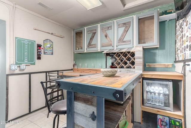 kitchen with light tile patterned floors, visible vents, butcher block counters, and glass insert cabinets