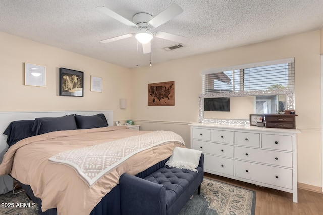 bedroom with visible vents, a textured ceiling, wood finished floors, and a ceiling fan