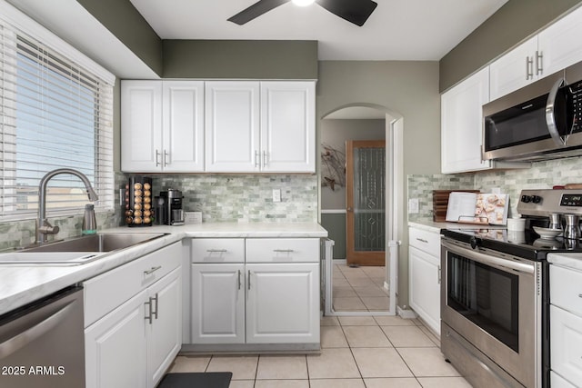 kitchen featuring light countertops, appliances with stainless steel finishes, light tile patterned flooring, arched walkways, and a sink