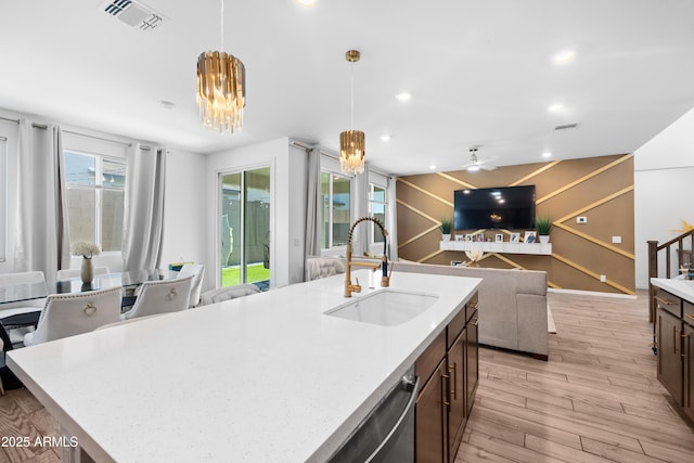 kitchen with sink, light stone counters, light hardwood / wood-style floors, an island with sink, and decorative light fixtures