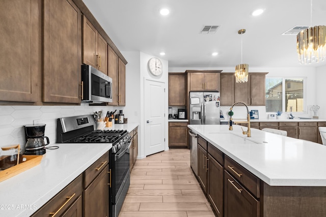 kitchen featuring sink, decorative light fixtures, stainless steel appliances, and a center island with sink