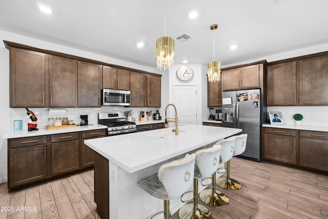 kitchen with an island with sink, sink, hanging light fixtures, light hardwood / wood-style floors, and stainless steel appliances