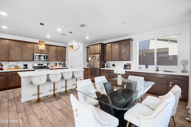 kitchen with a breakfast bar, appliances with stainless steel finishes, an island with sink, decorative light fixtures, and light wood-type flooring