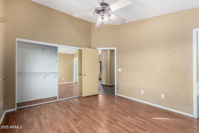 unfurnished bedroom featuring wood-type flooring, a towering ceiling, ceiling fan, and a closet