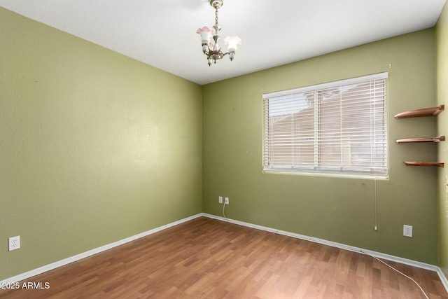 spare room with hardwood / wood-style flooring and an inviting chandelier