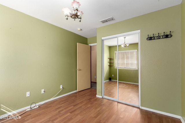 unfurnished bedroom featuring an inviting chandelier, hardwood / wood-style flooring, and a closet