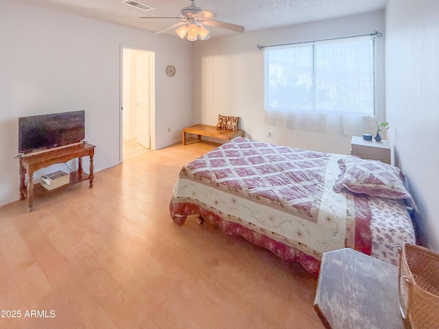 bedroom featuring ceiling fan, wood finished floors, visible vents, and a textured ceiling