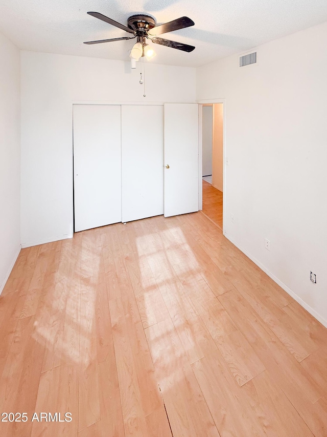 unfurnished bedroom with visible vents, light wood-style flooring, a closet, a textured ceiling, and a ceiling fan