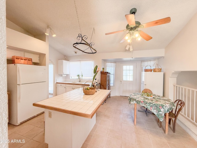 kitchen with a textured ceiling, tile counters, vaulted ceiling, and freestanding refrigerator