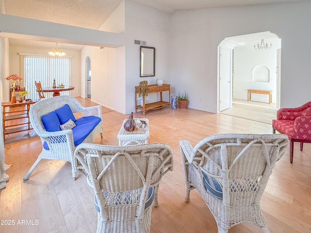 living area featuring visible vents, arched walkways, light wood-style floors, an inviting chandelier, and vaulted ceiling