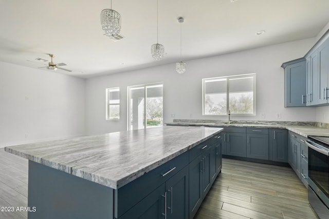 kitchen with stainless steel electric range oven, a kitchen island, hanging light fixtures, and ceiling fan with notable chandelier