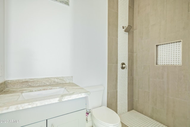 bathroom featuring a tile shower, vanity, and toilet