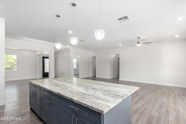 kitchen featuring hardwood / wood-style floors, a kitchen island, pendant lighting, and ceiling fan with notable chandelier