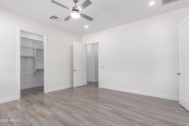 unfurnished bedroom featuring a closet, a walk in closet, light hardwood / wood-style floors, and ceiling fan