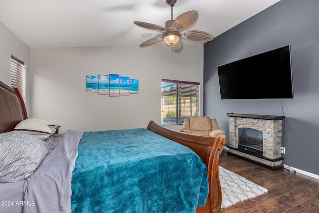 bedroom with ceiling fan, dark hardwood / wood-style floors, vaulted ceiling, and a stone fireplace