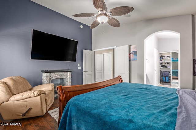 bedroom featuring a stone fireplace, dark wood-type flooring, a closet, and ceiling fan