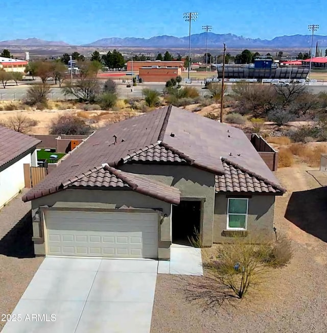 view of front of property featuring stucco siding, driveway, a tile roof, a mountain view, and an attached garage