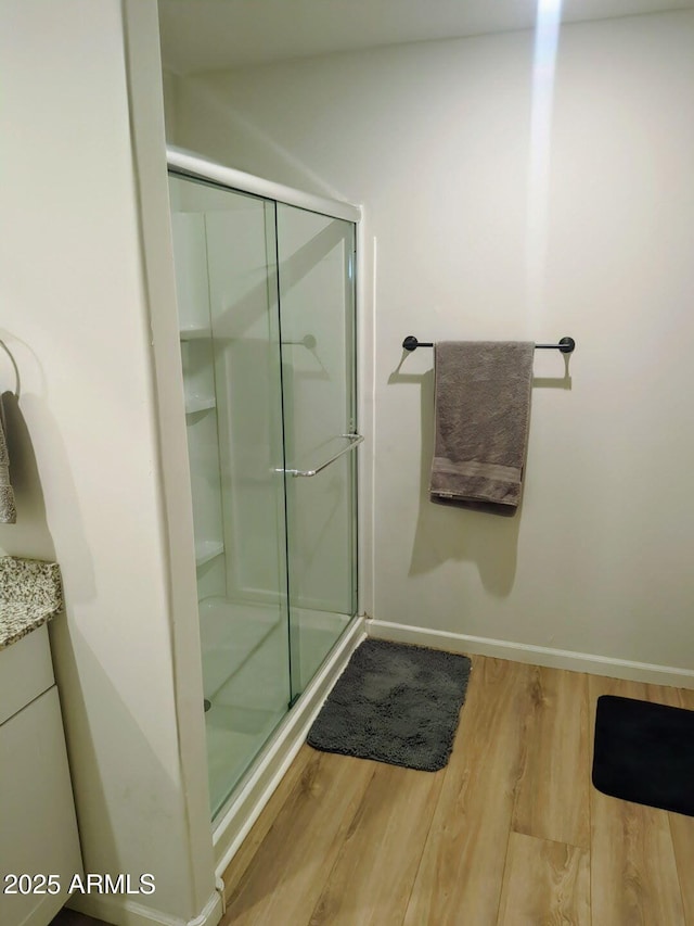 full bath featuring baseboards, wood finished floors, a stall shower, and vanity