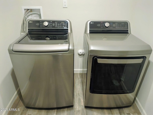 washroom with washing machine and clothes dryer, laundry area, baseboards, and wood finished floors