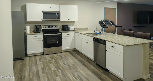 kitchen with a sink, white cabinetry, appliances with stainless steel finishes, a peninsula, and light wood finished floors