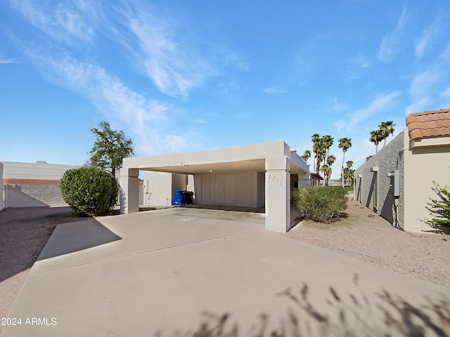 exterior space with a carport, concrete driveway, fence, and stucco siding