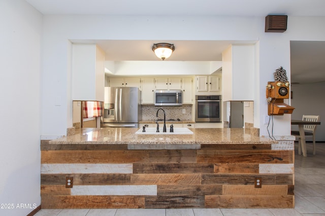 kitchen featuring appliances with stainless steel finishes, sink, backsplash, and light stone counters