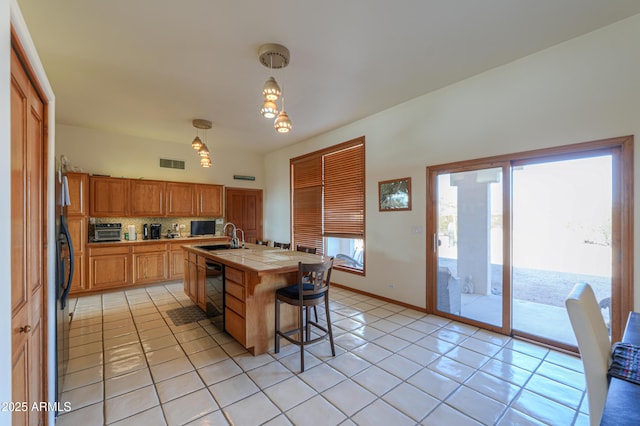 kitchen with tile countertops, decorative light fixtures, black dishwasher, sink, and light tile patterned floors