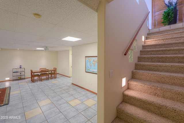 stairway featuring a paneled ceiling, tile patterned floors, and ceiling fan