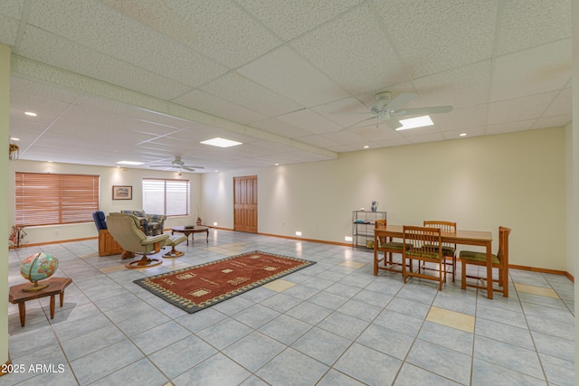 living room with ceiling fan, a paneled ceiling, and light tile patterned floors