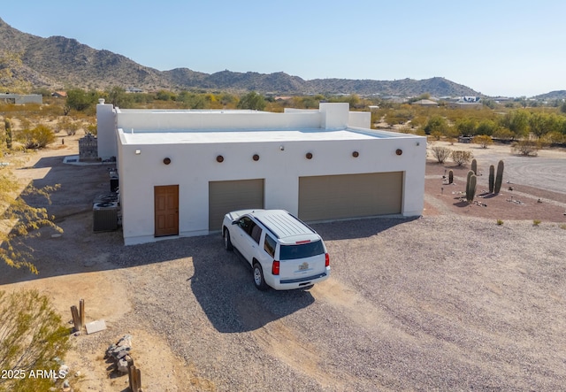 pueblo-style house featuring a garage, a mountain view, and central air condition unit